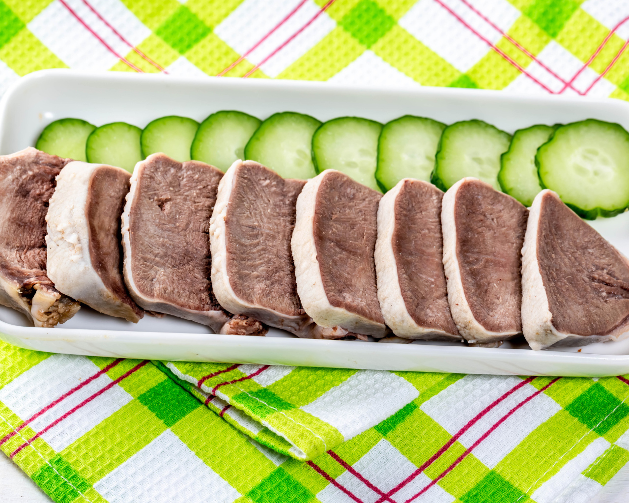Вареный язык на тарелке со свежими огурцами