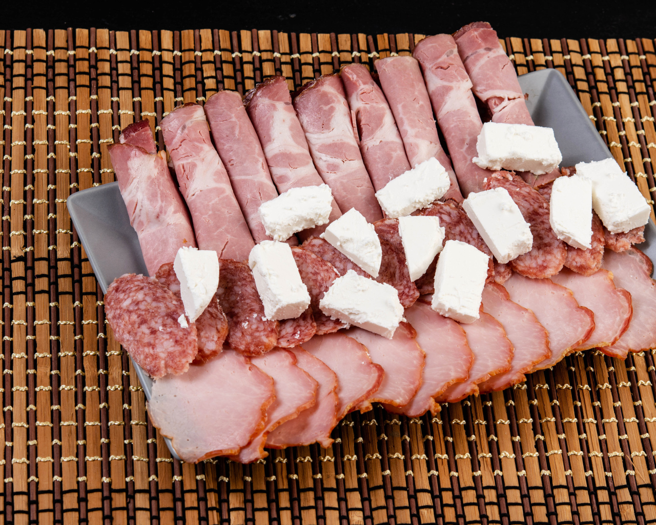 Колбаса и ветчина на тарелке с кусочками сыра фета