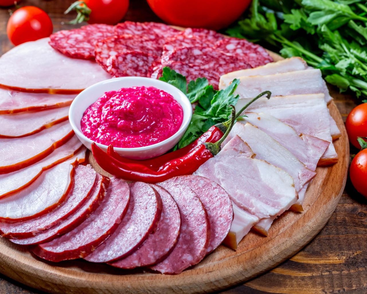 Мясная нарезка на доске с соусом, красным перцем,  помидорами и зеленью 