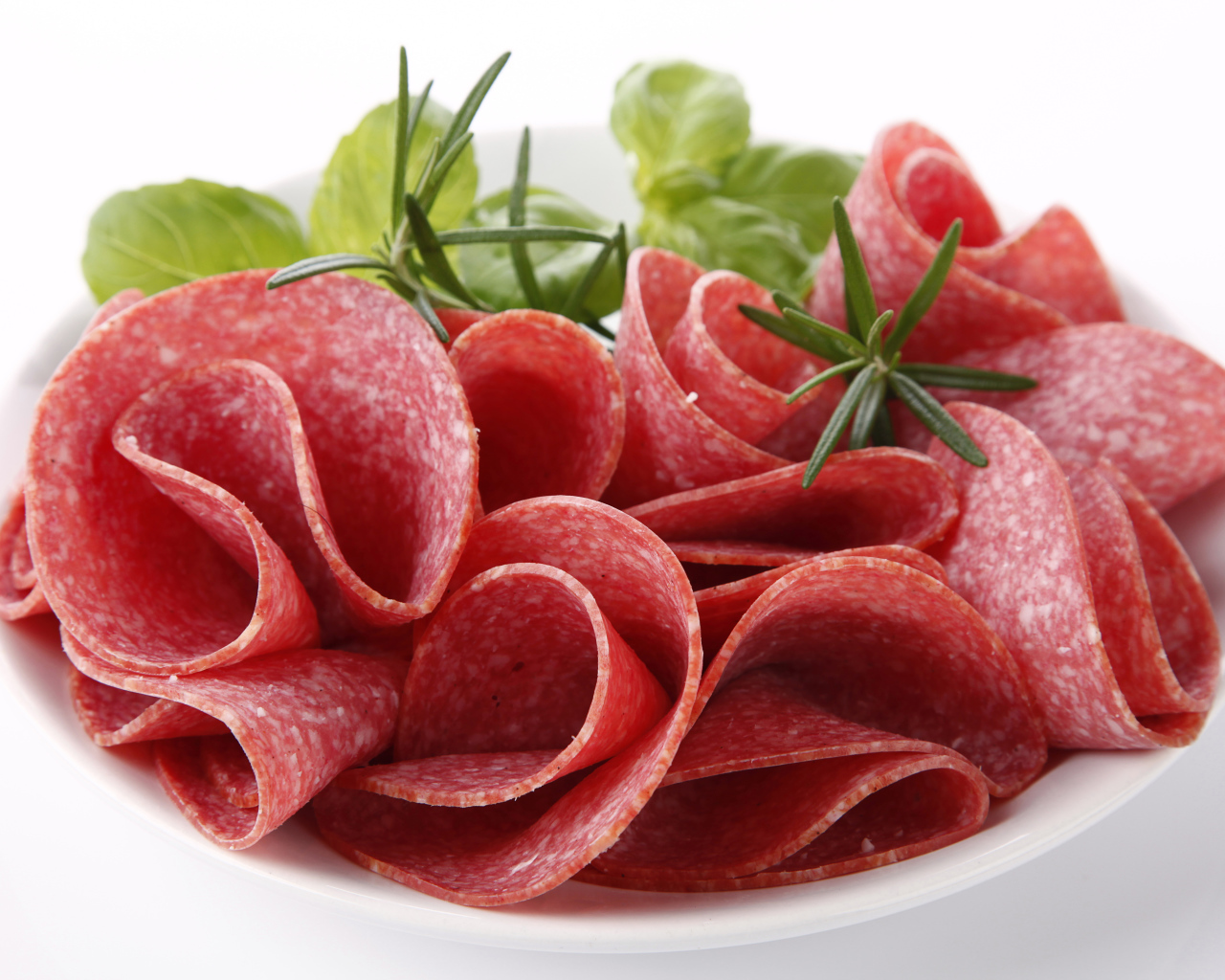 Тонкие кусочки колбасы на тарелке с зеленью 