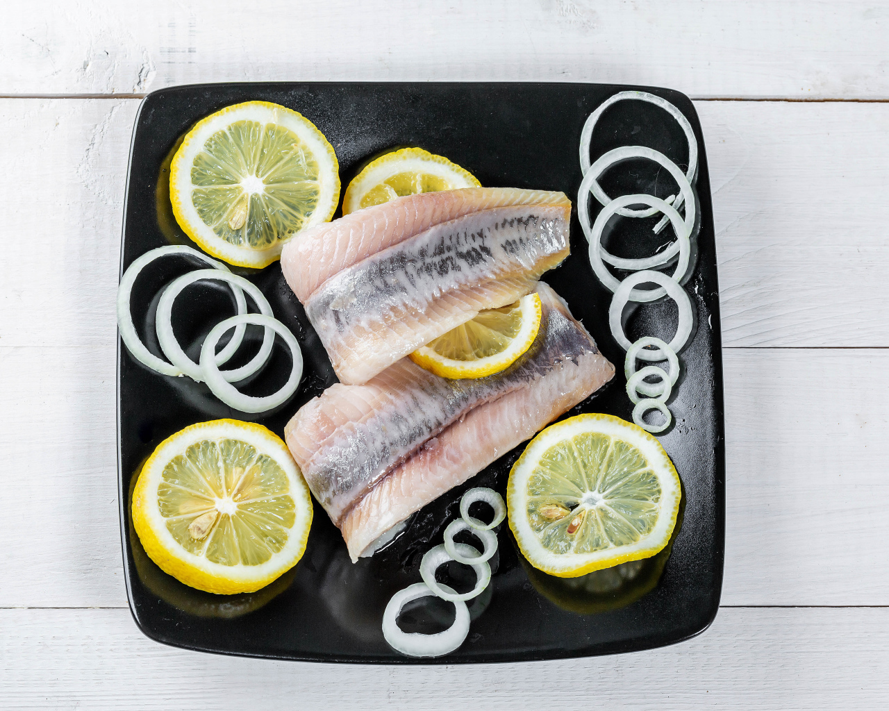 Филе сельди на черной тарелке с луком и лимоном