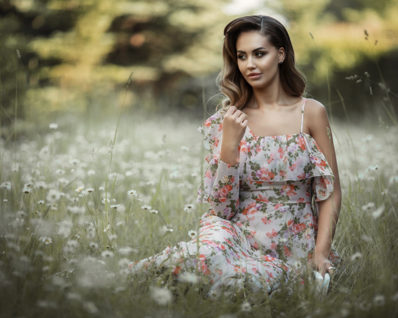 Красивая девушка в сарафане сидит на поляне с ромашками 