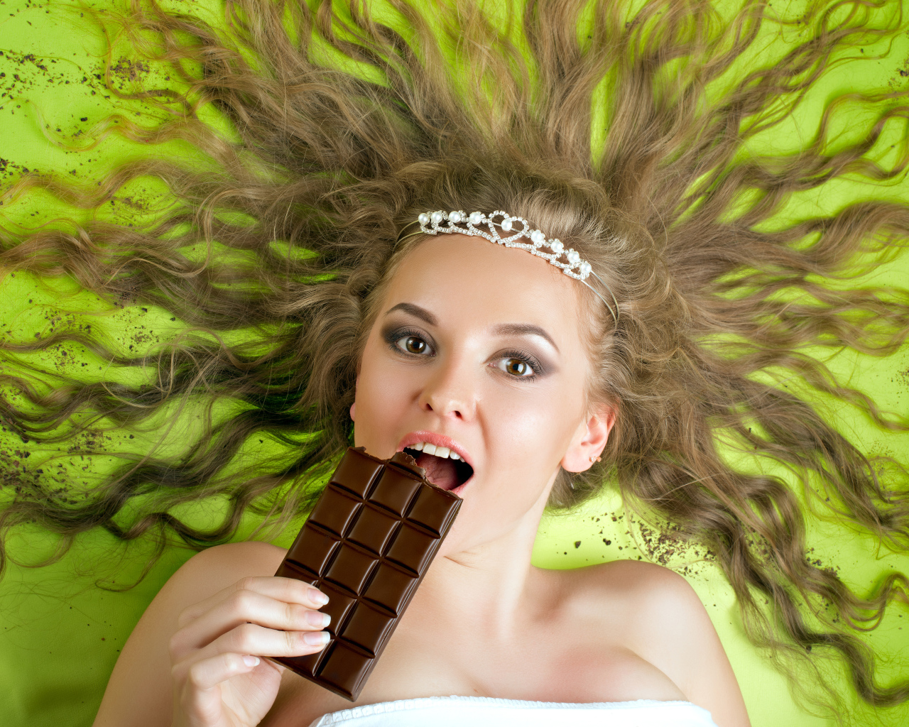 Красивая девушка с украшением в волосах лежит с шоколадкой 