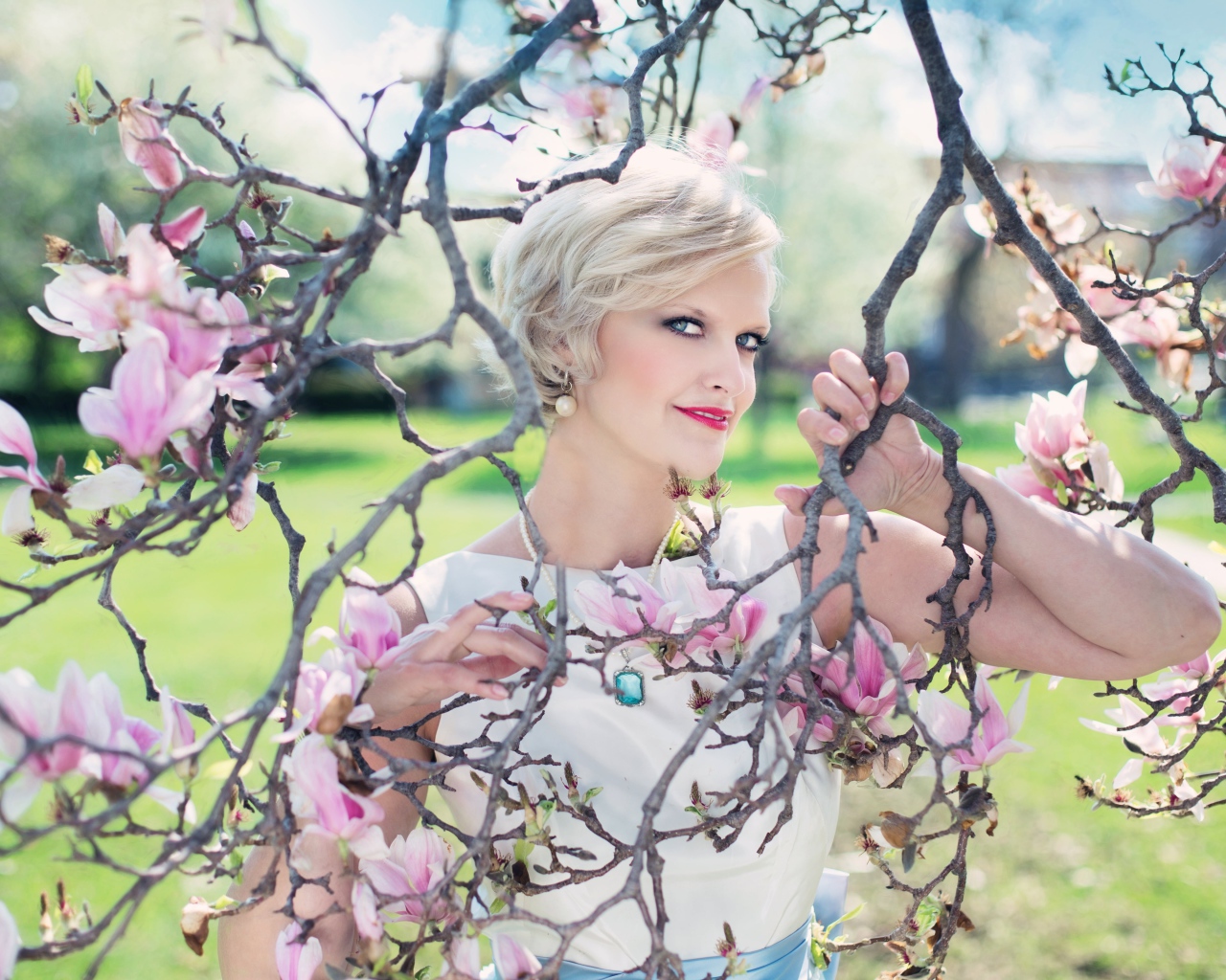 Красивая женщина с короткой стрижкой стоит у цветущей магнолии 