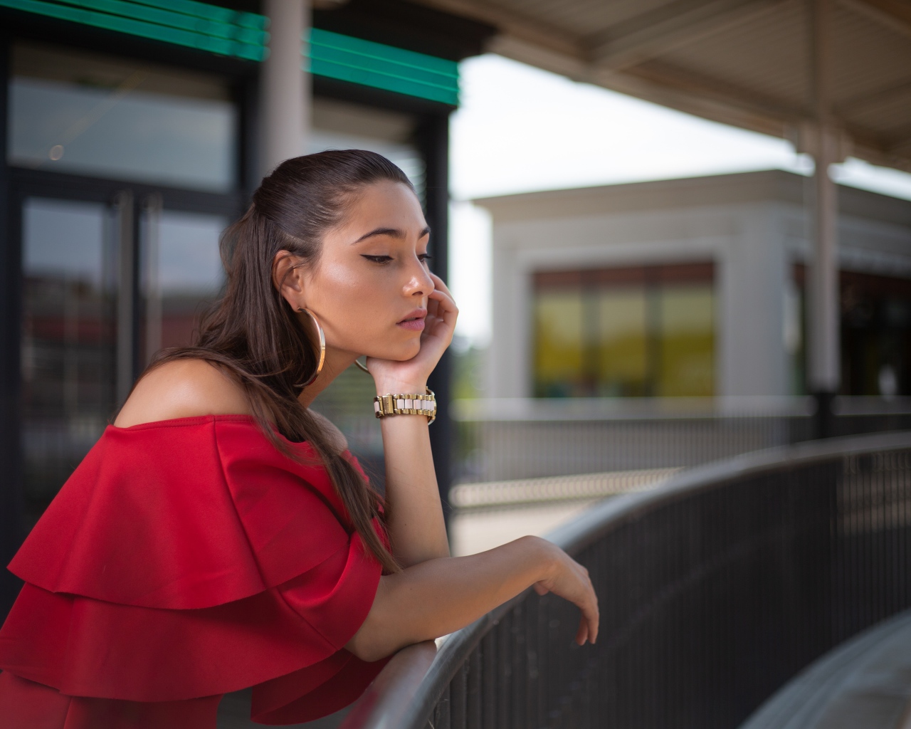 Задуманная девушка в красном платье стоит у перил 