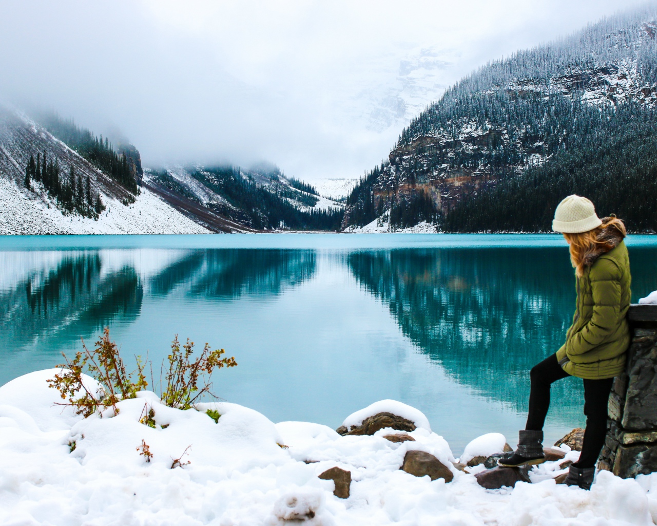 Девушка стоит у голубого озера на заснеженном берегу 