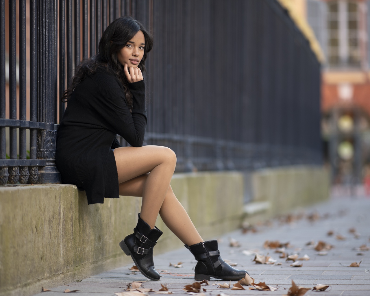 Молодая девушка в черном сидит у железного забора