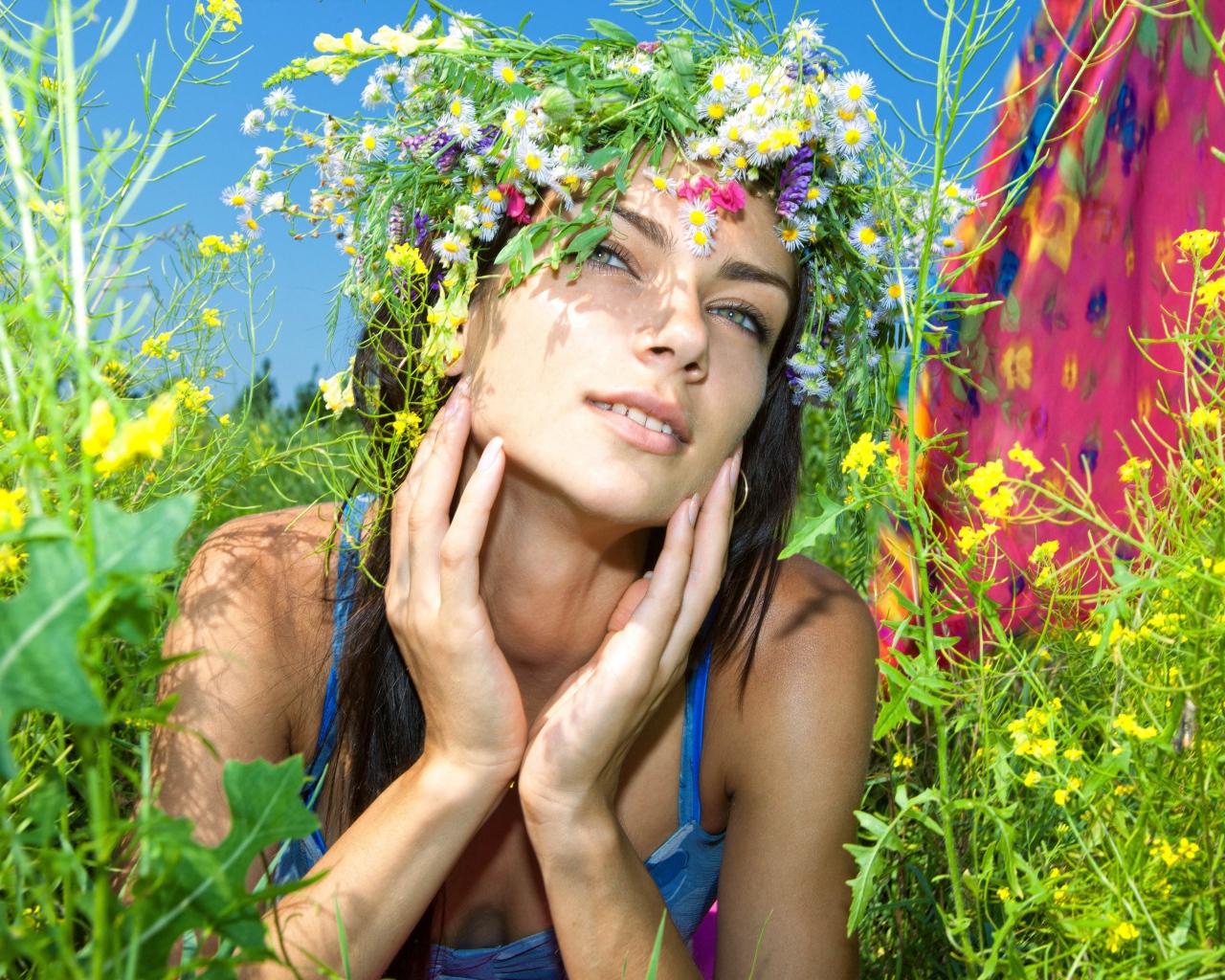 Молодая девушка с венком из полевых цветов лежит в траве