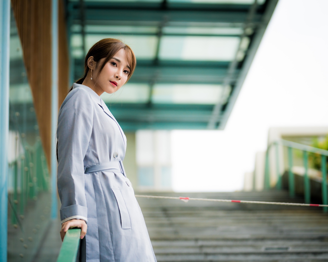 Девушка азиатка в пальто стоит у перил 