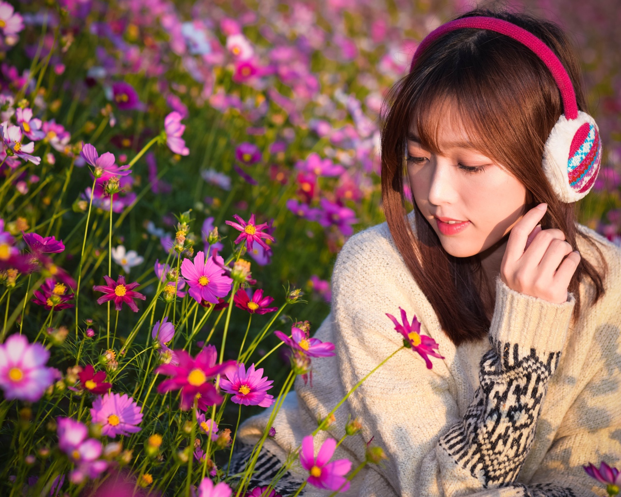 Девушка азиатка в наушниках сидит в цветах космеи