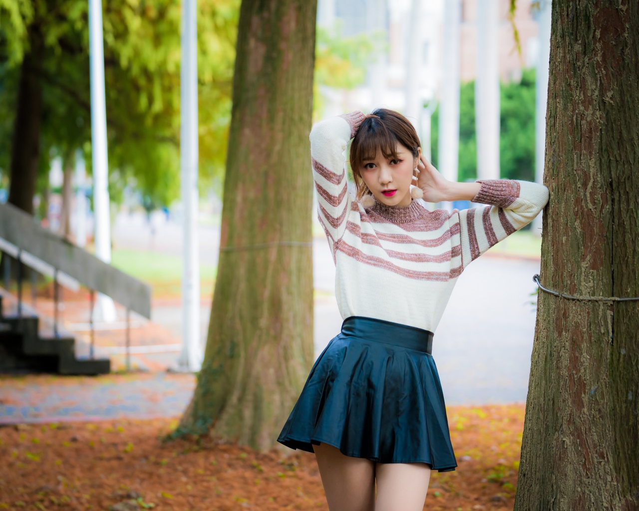 Девушка азиатка стоит в короткой юбке у дерева