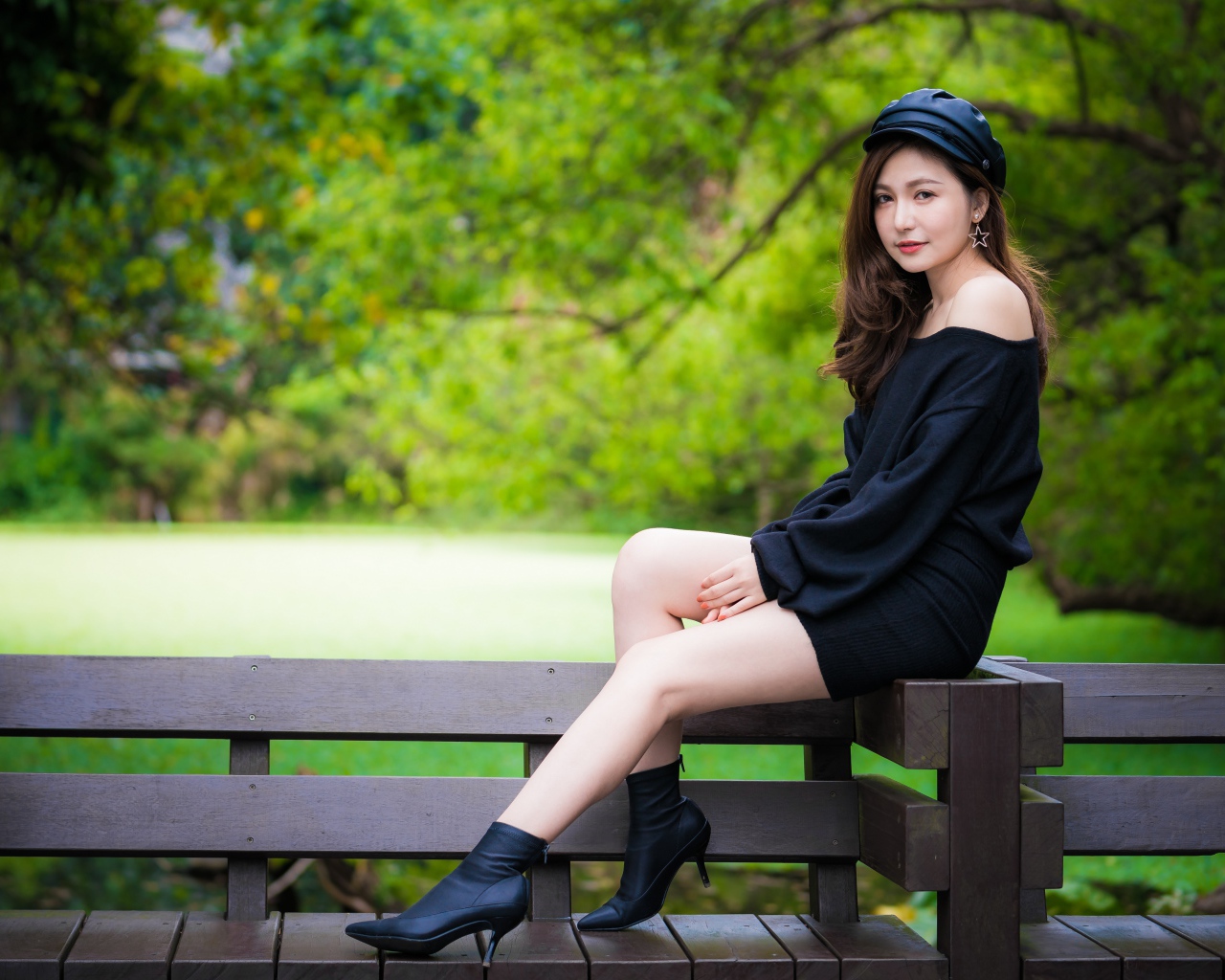 Красивая девушка азиатка в черном платье сидит на деревянной лавке