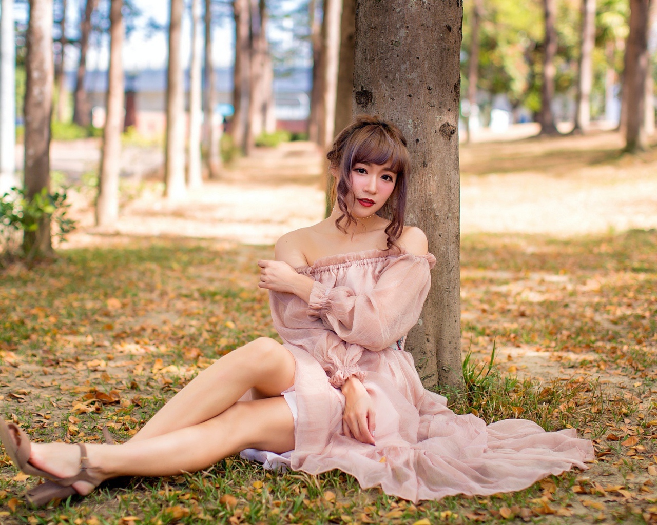 Красивая девушка азиатка в платье сидит под деревом