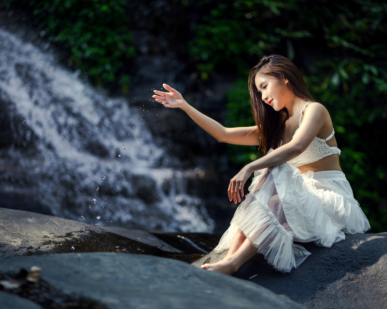 Красивая девушка азиатка в белом платье сидит у воды