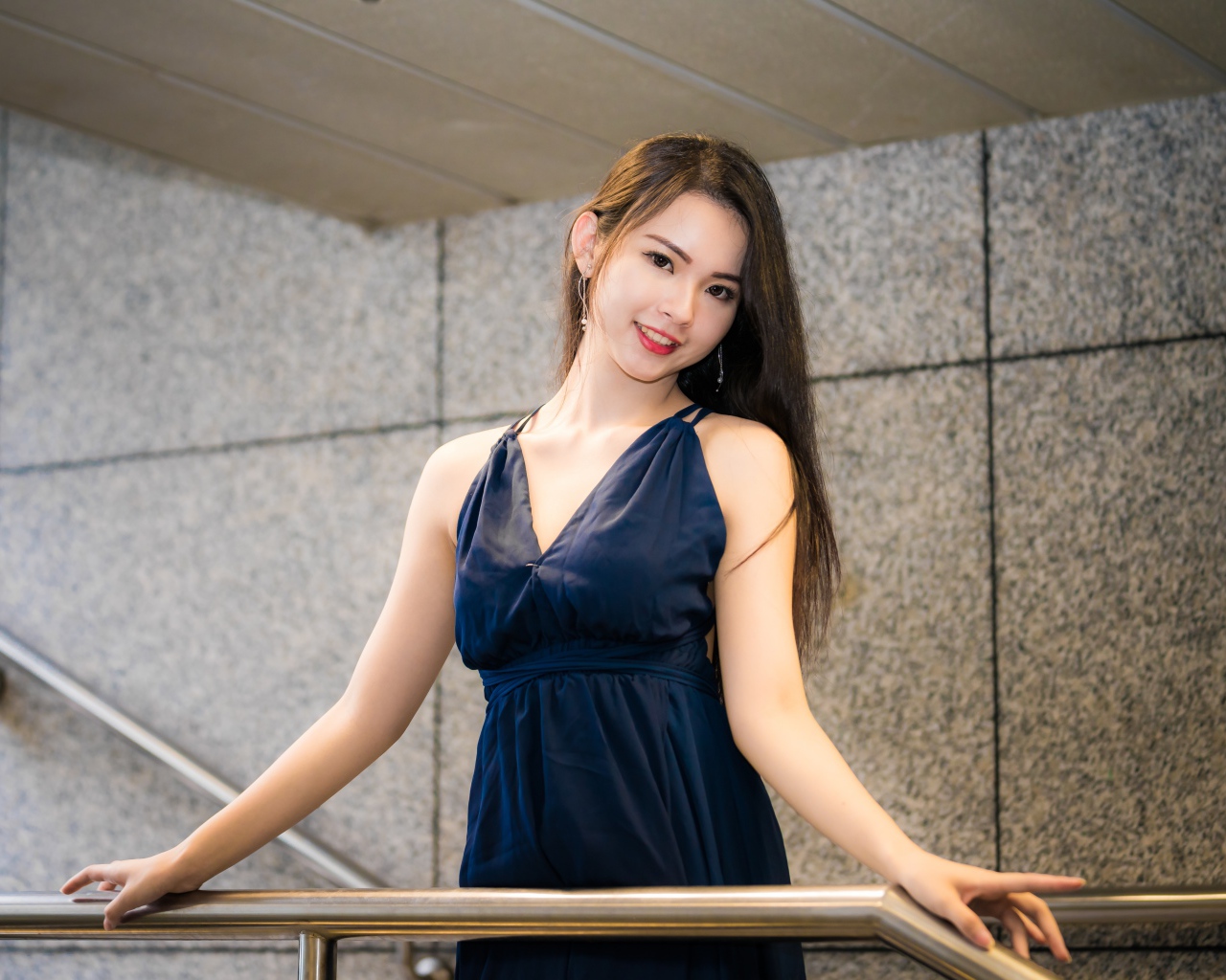 Красивая азиатка в черном платье стоит у перил