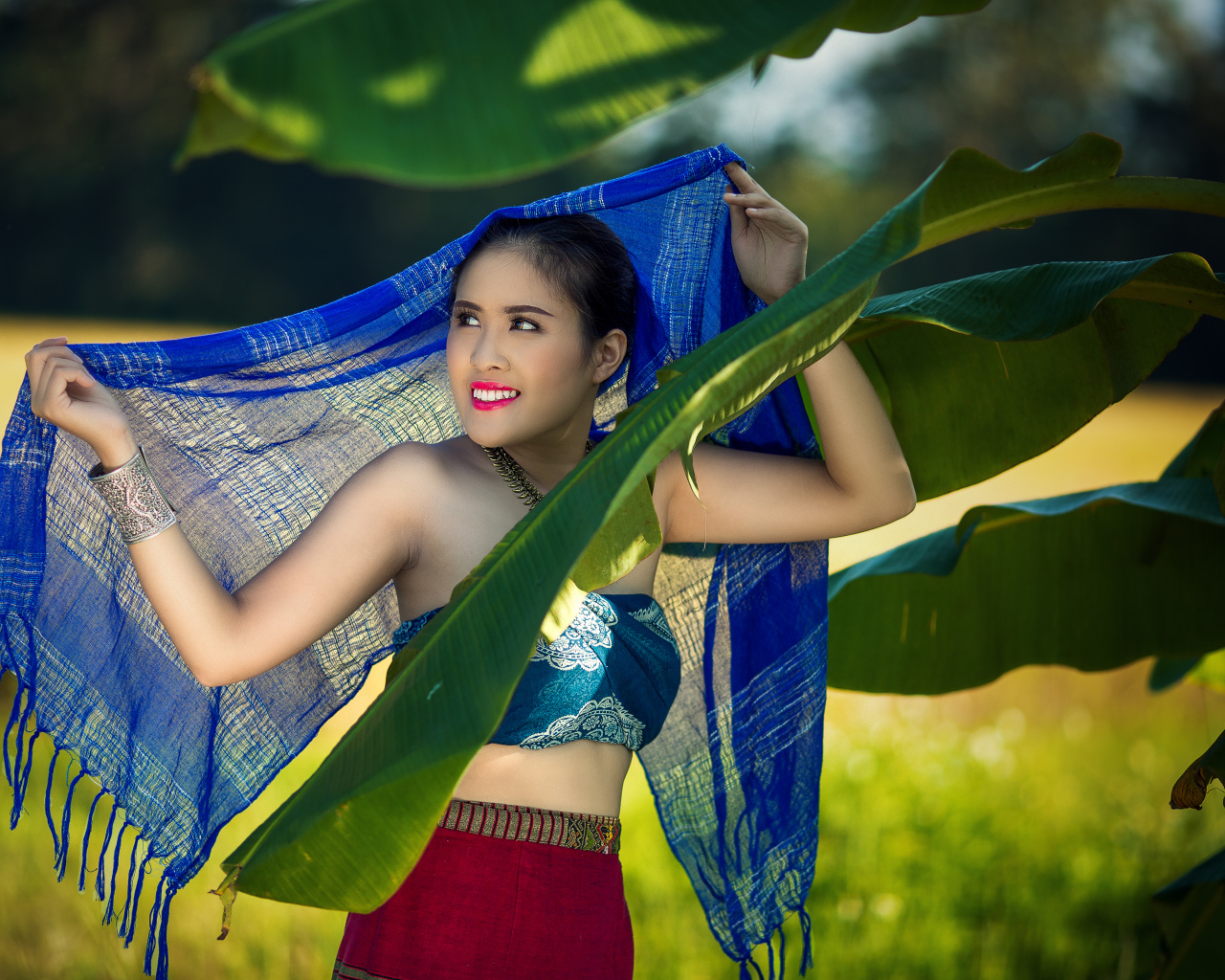 Красивая девушка азиатка с синим палантином у зеленых листьев