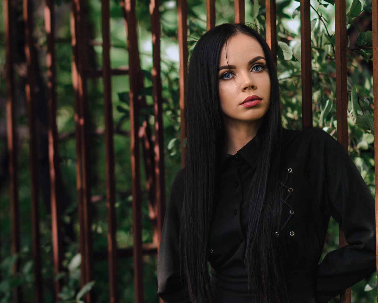 Красивая голубоглазая девушка в черном платье у железного забора