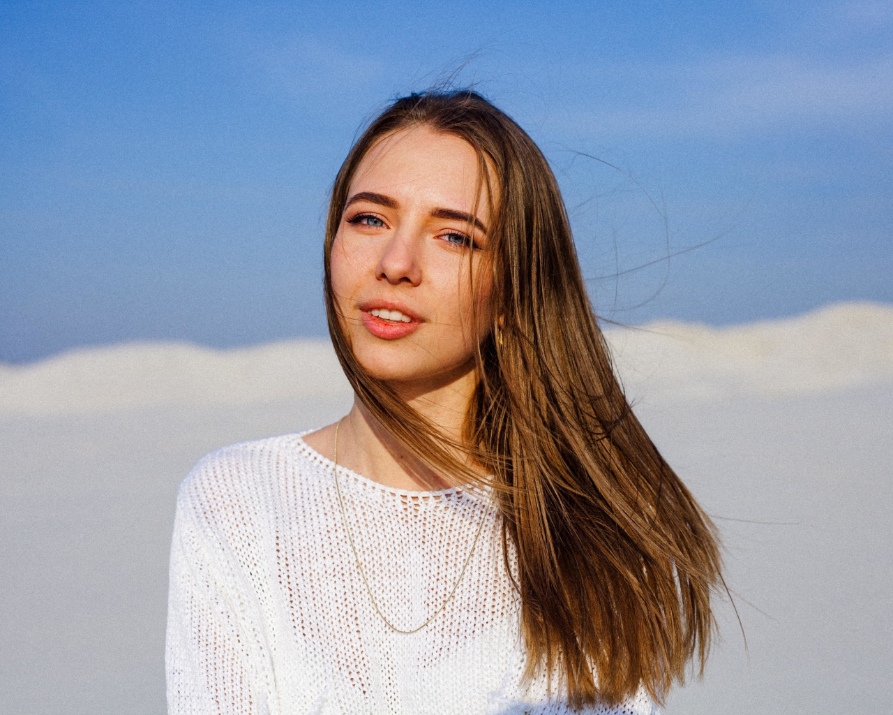 Красивая голубоглазая девушка в белом свитере на фоне голубого неба