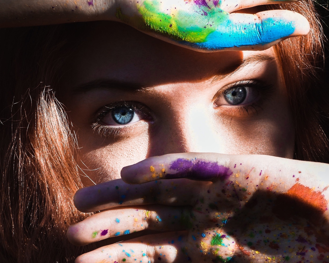 Красивая голубоглазая девушка с руками в разноцветной краске у лица