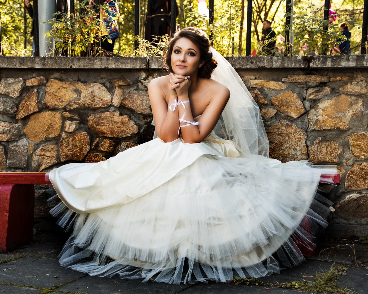 Красивая невеста в белом платье сидит на лавке