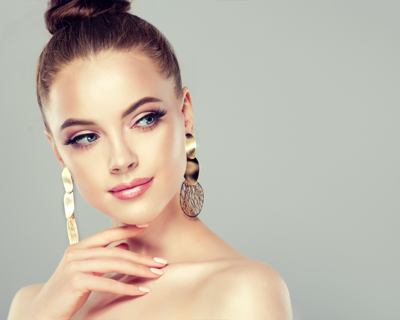 Красивая девушка шатенка с золотыми серьгами в ушах на сером фоне