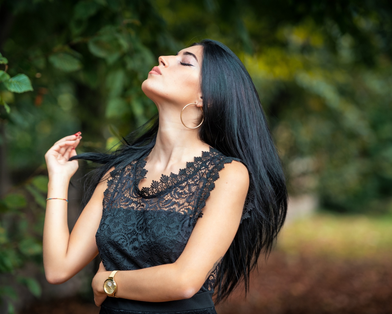 Красивая брюнетка в черном платье с закрытыми глазами в парке