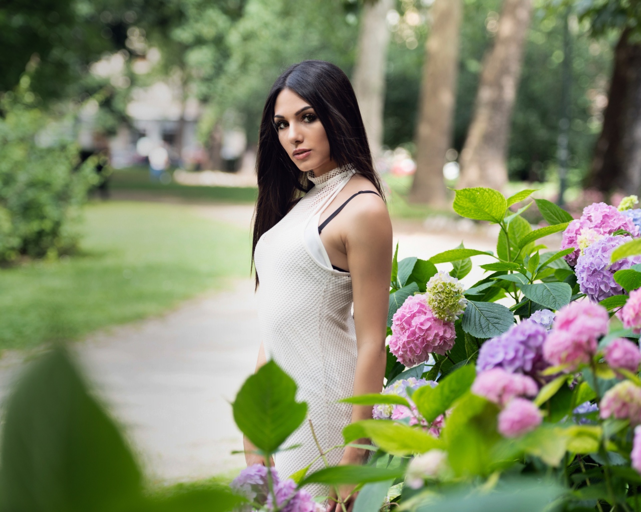 Красивая брюнетка стоит рядом с кустом гортензии