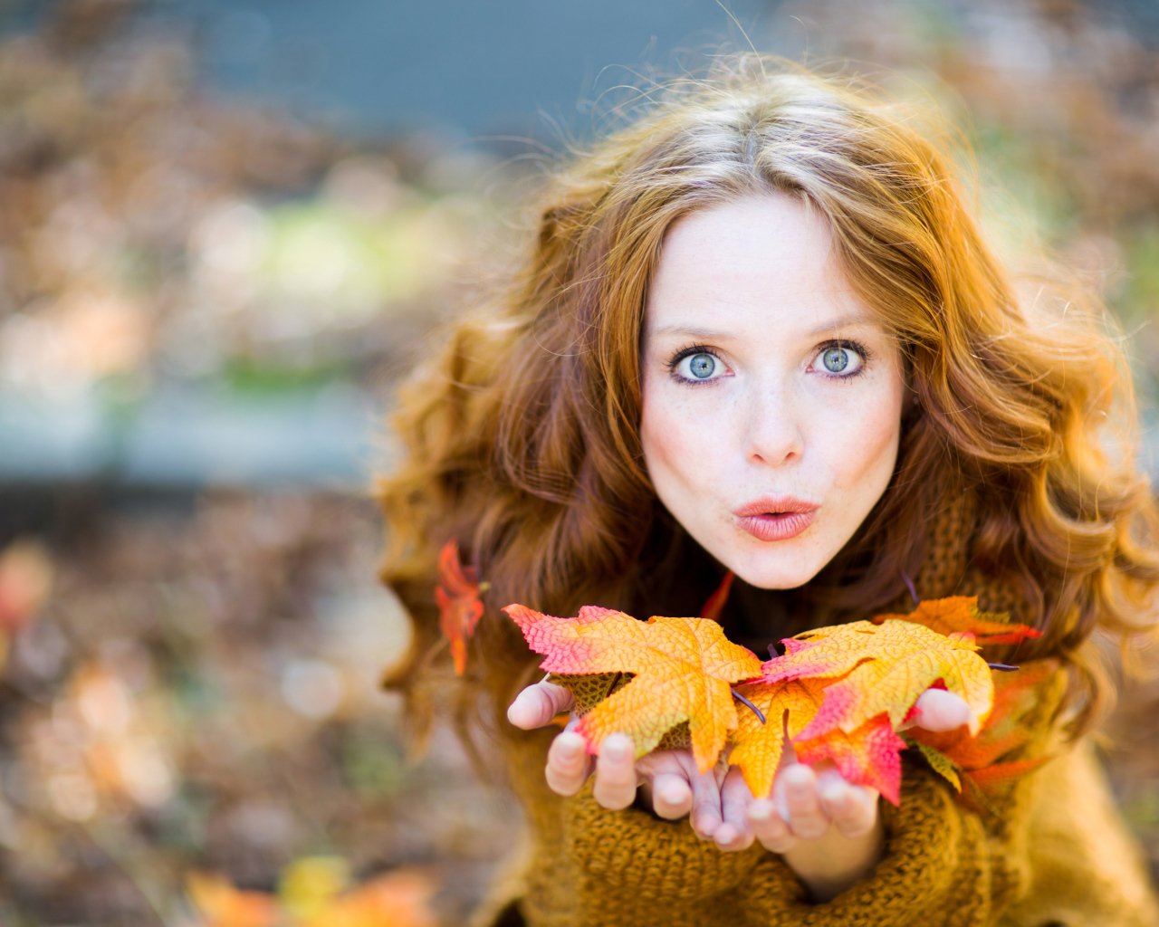 Красивая девушка сдувает листья с ладоней