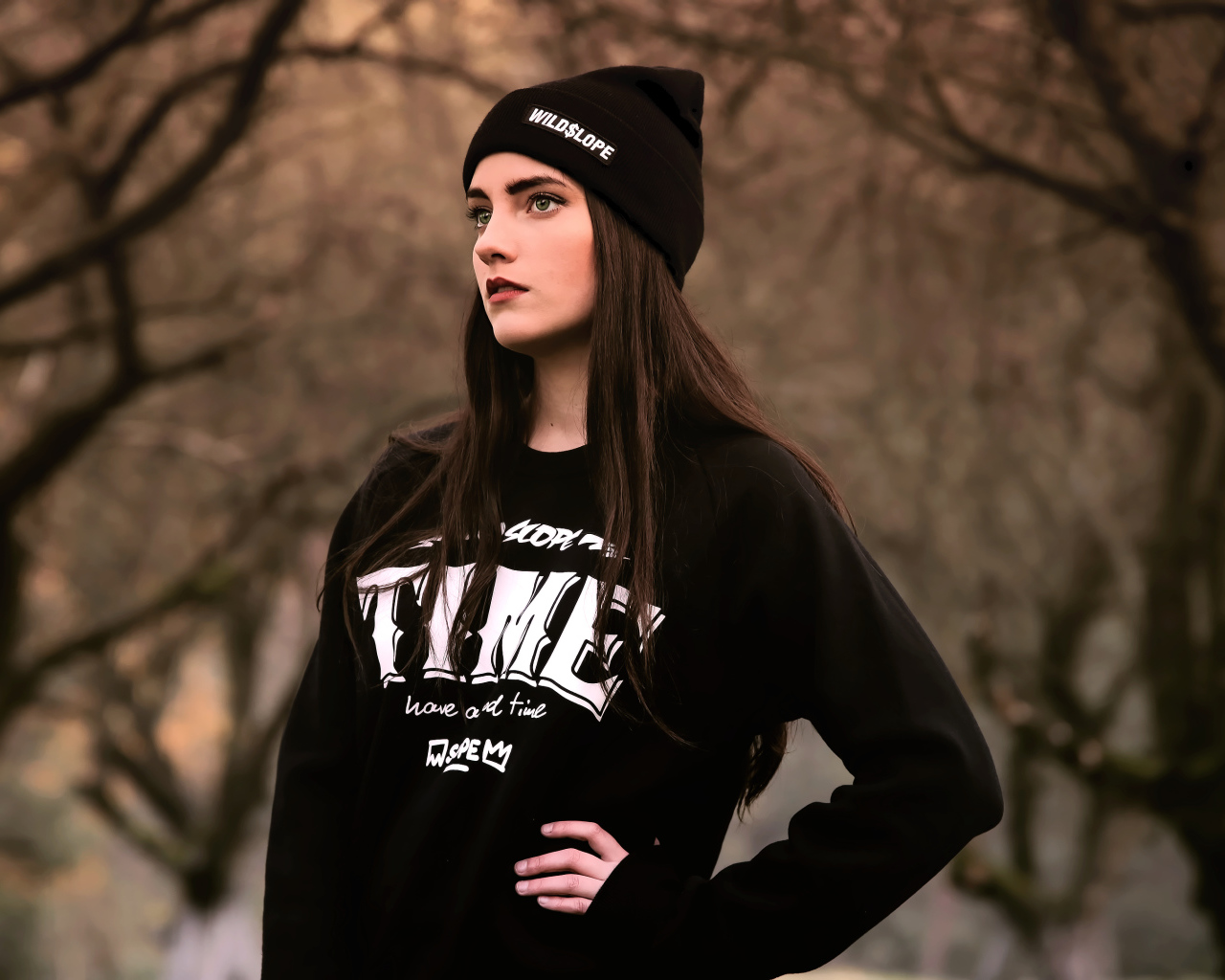 Красивая девушка в черной шапке у деревьев 