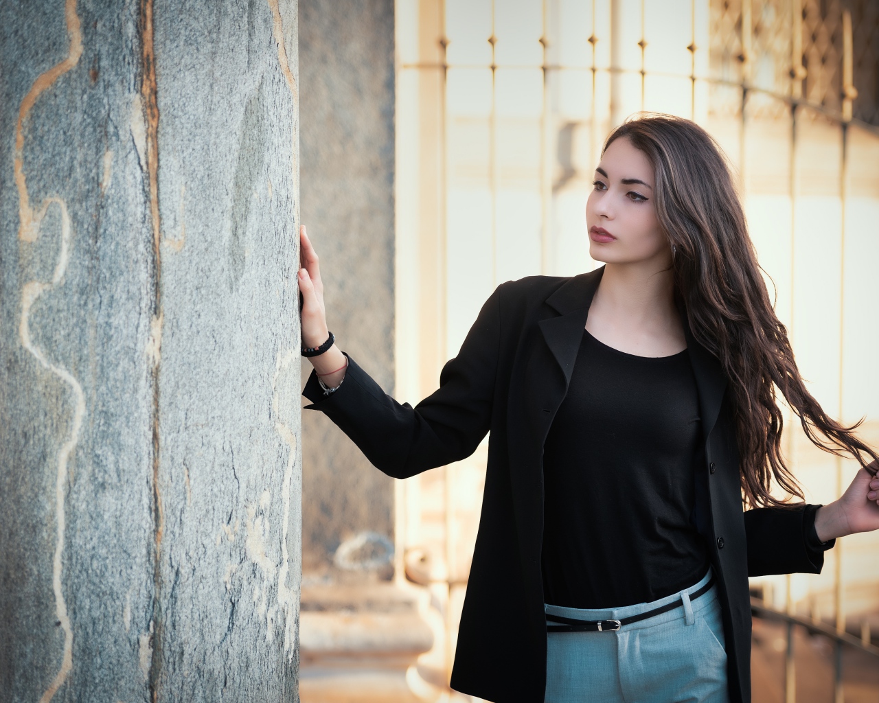 Красивая девушка в черном пиджаке стоит у стены