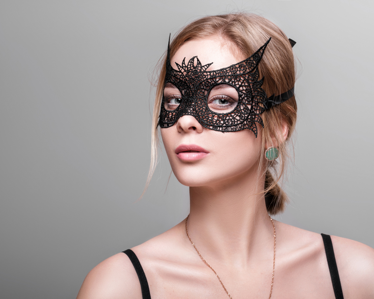 Красивая девушка в черной маске на сером фоне
