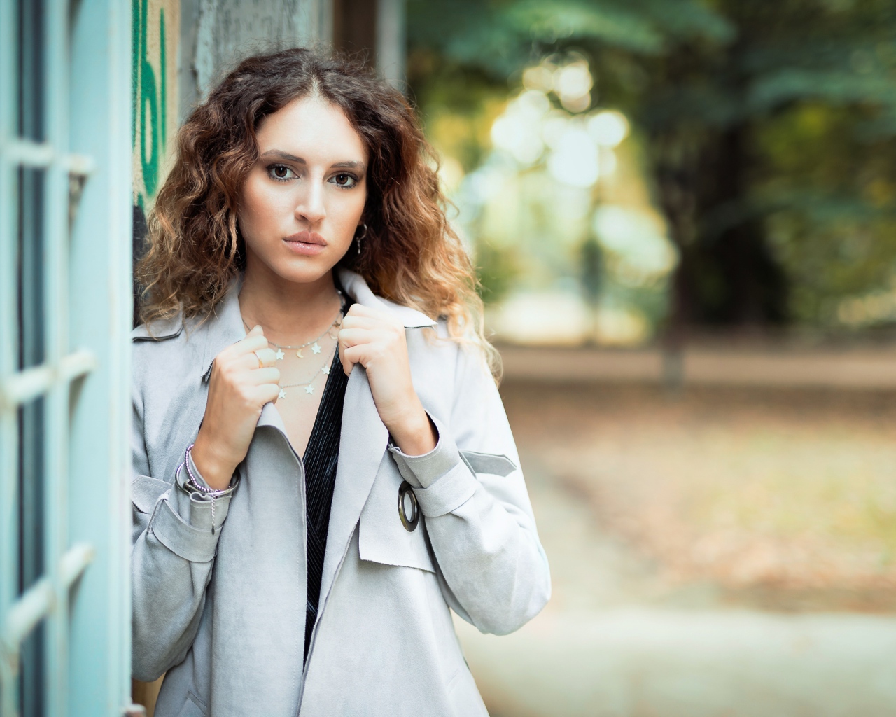 Красивая девушка в сером плаще у стены