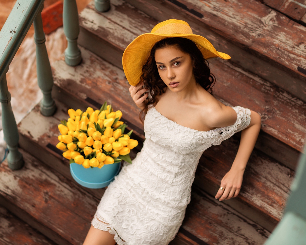 Красивая девушка в белом платье и желтой шляпе на ступеньках с букетом тюльпанов