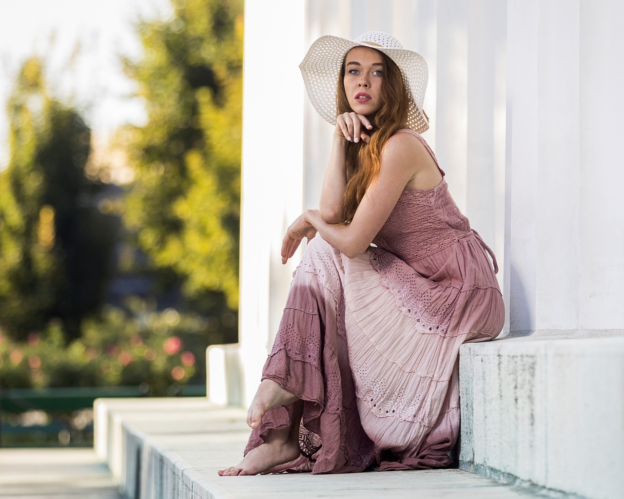 Красивая девушка в белой шляпе сидит на ступеньках 