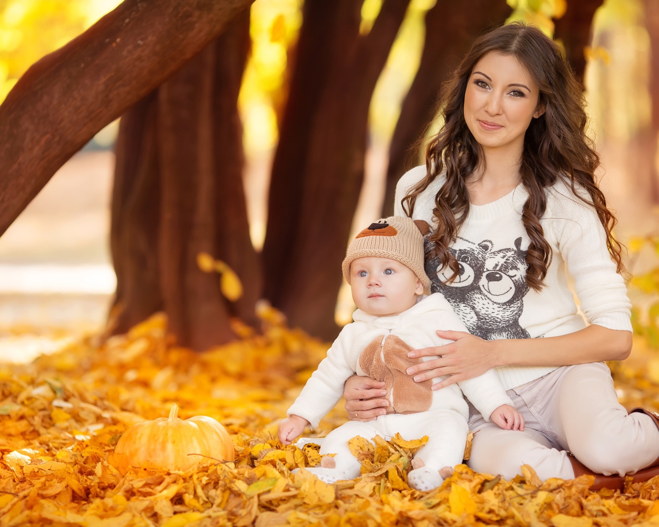 Красивая девушка сидит с грудным ребенком на опавшей листве
