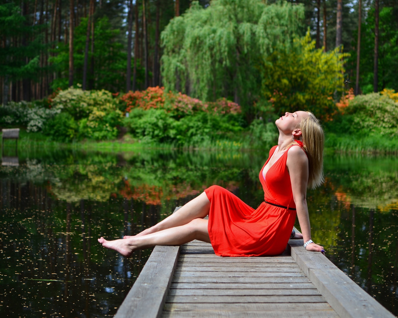 Красивая девушка сидит в красном платье на мосту