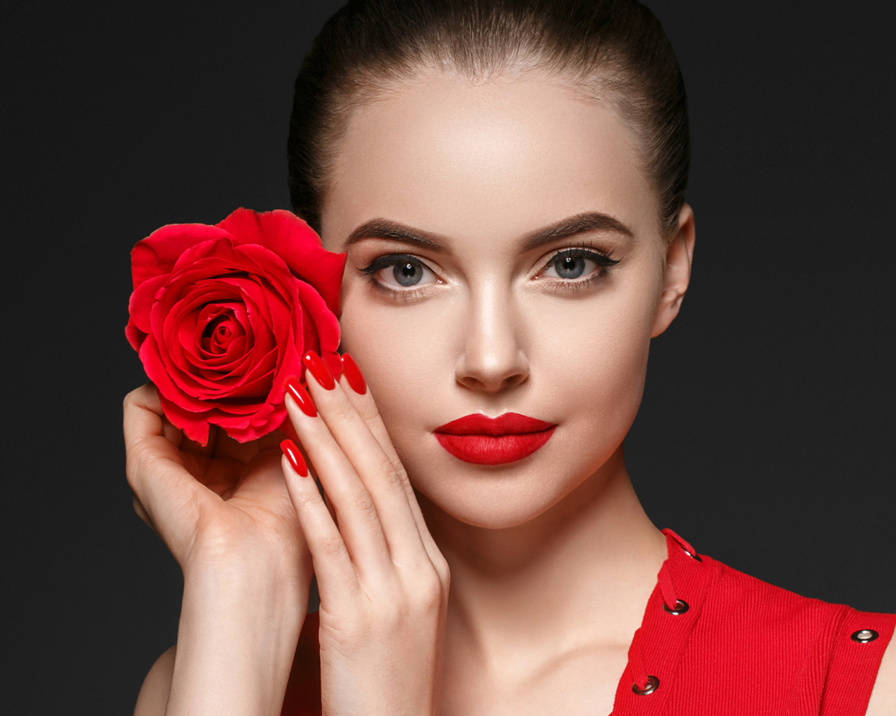 Красивая девушка с красной розой у лица на сером фоне