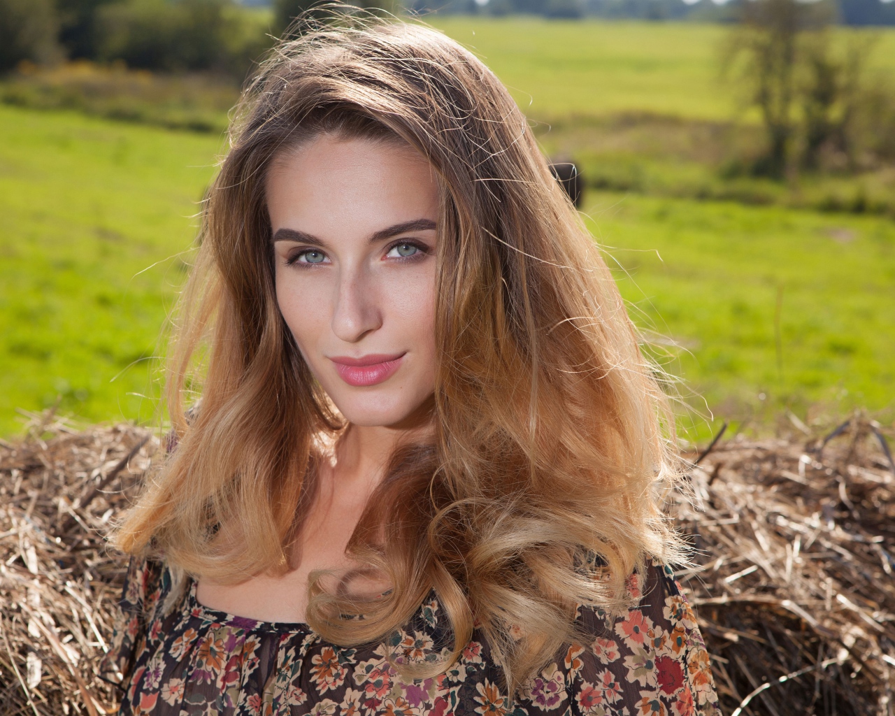 Красивая девушка с серыми глазами стоит у сена