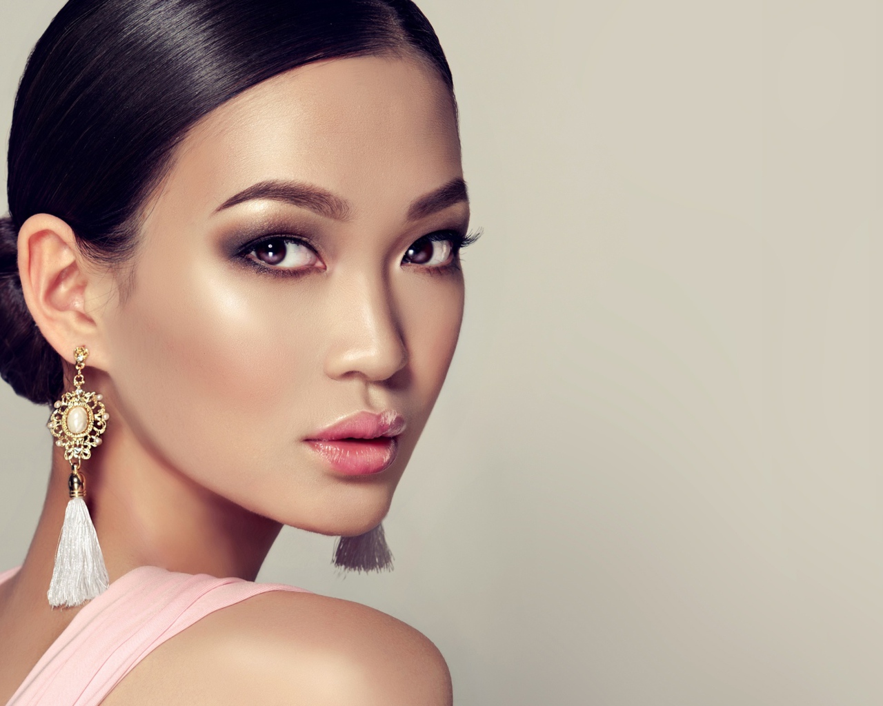 Красивая девушка с прической и сережками в ушах на сером фоне