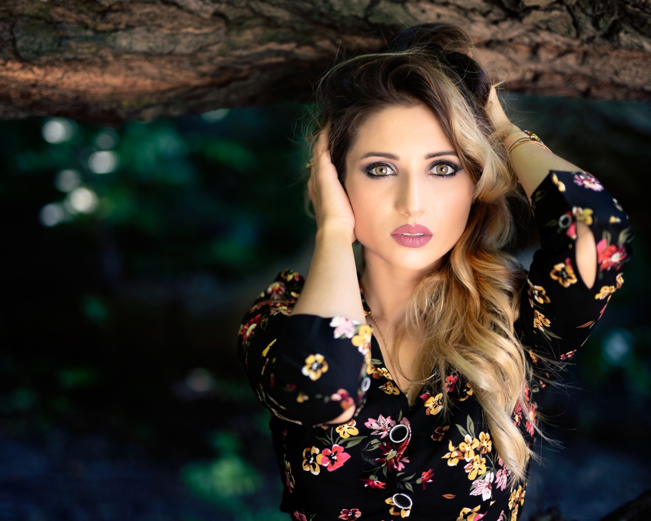 Красивая девушка с руками в волосах у дерева