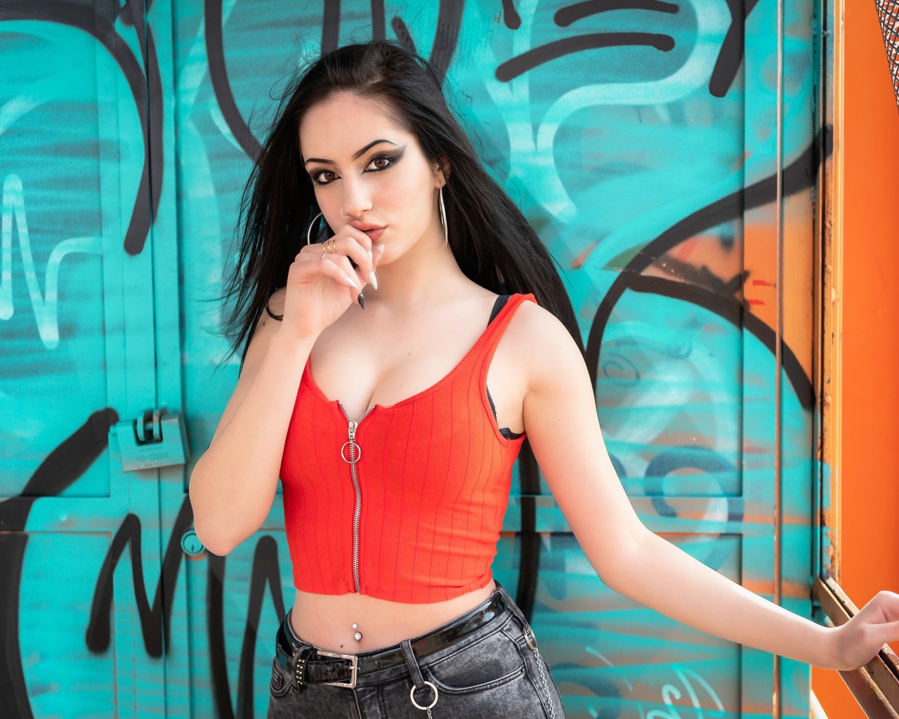 Красивая девушка с пирсингом стоит у стены