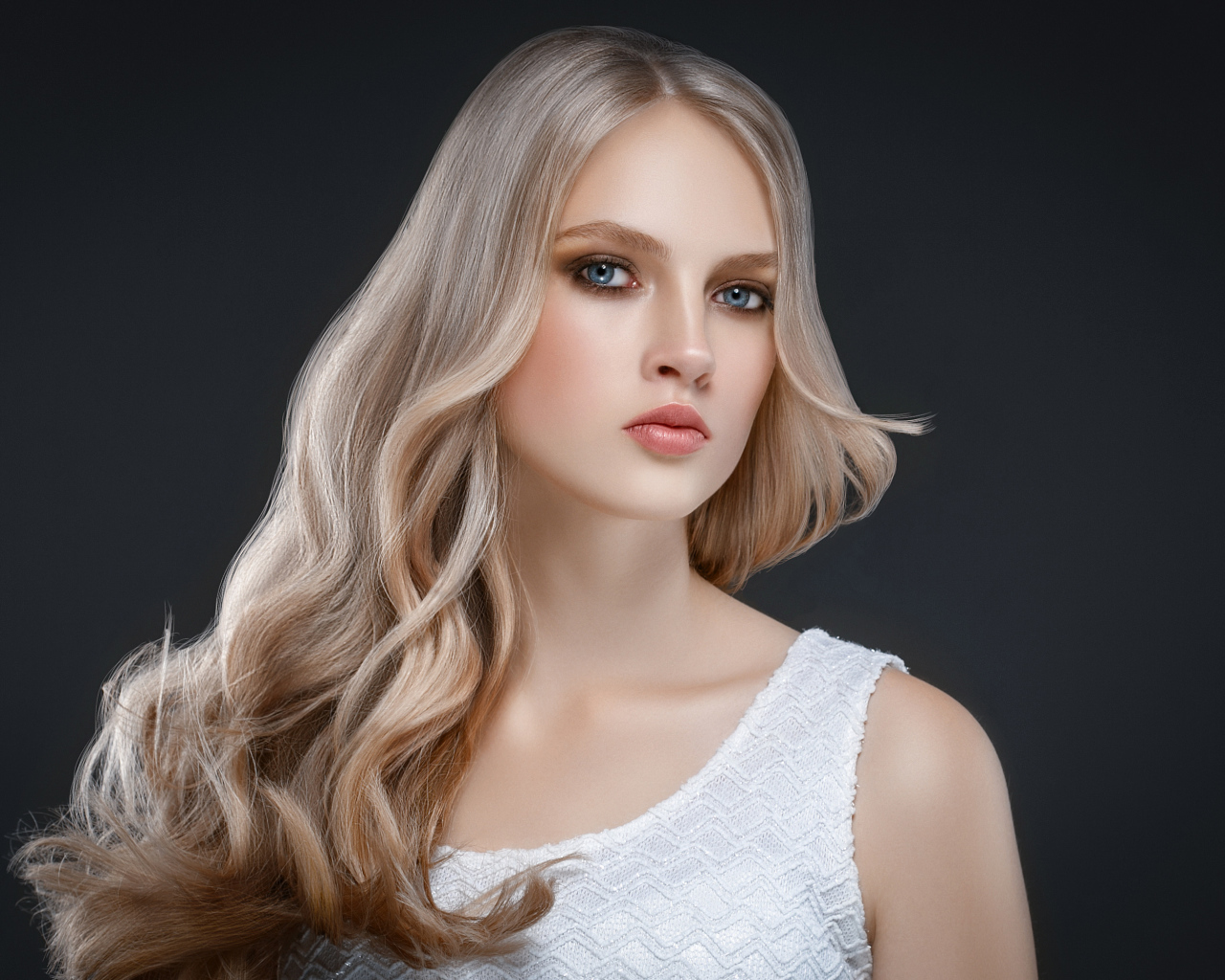 Красивая длинноволосая блондинка с голубыми глазами на сером фоне