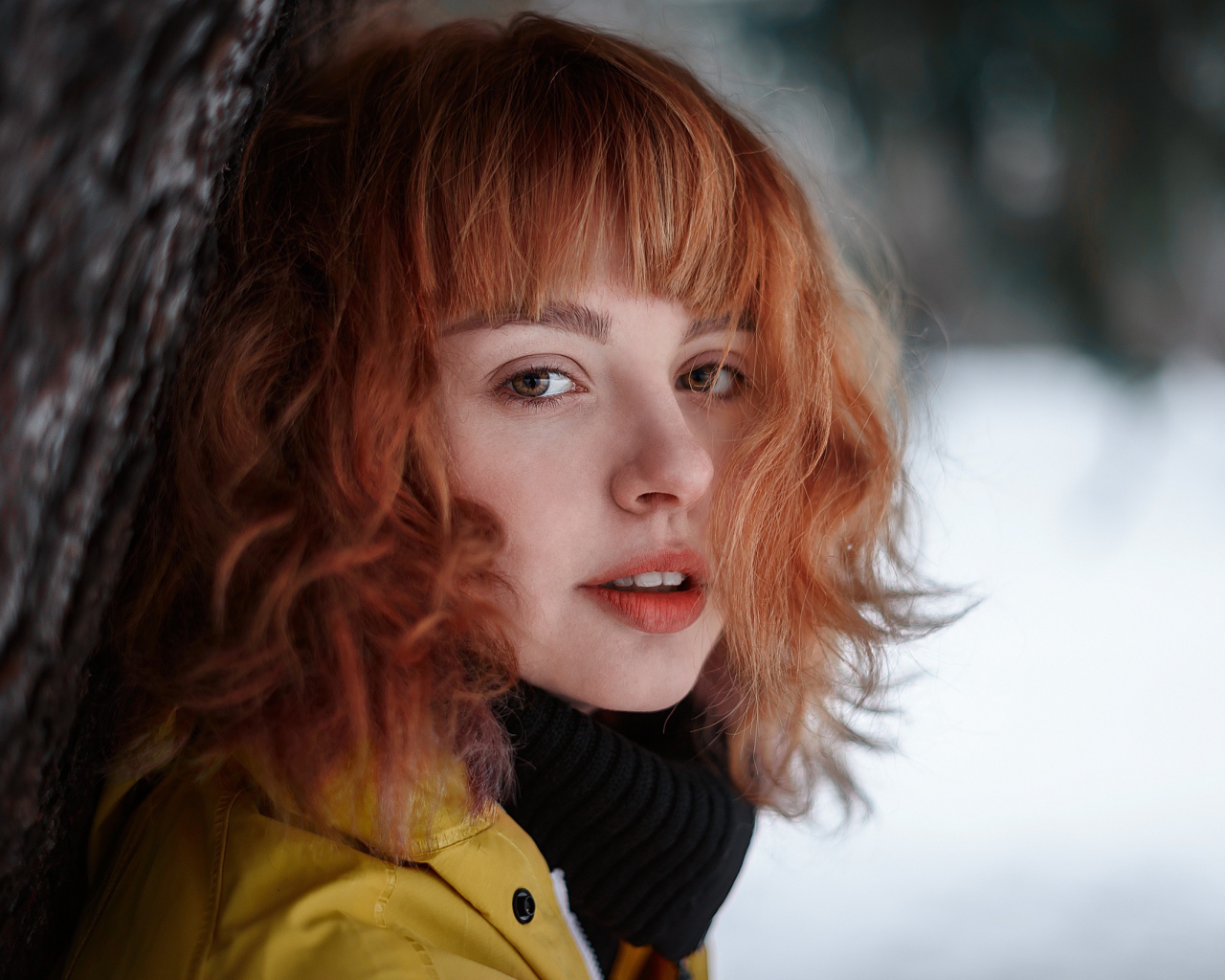 Красивая рыжеволосая девушка стоит у дерева зимой