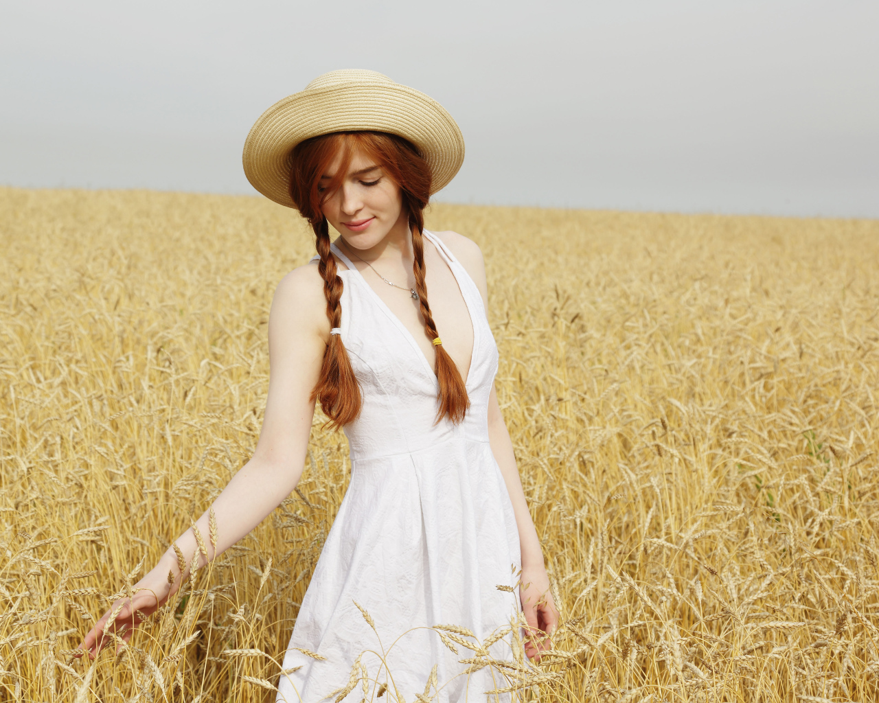 Красивая рыжеволосая девушка гуляет по полю с пшеницей