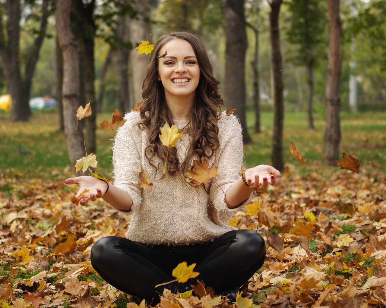 Красивая улыбающаяся девушка сидит на земле с желтыми листьями