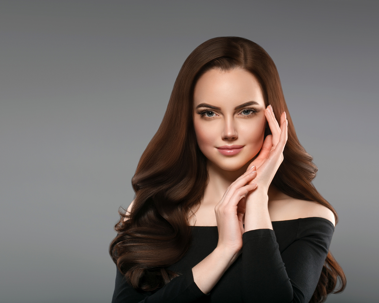 Красивая нежная длинноволосая шатенка  с руками у лица на сером фоне