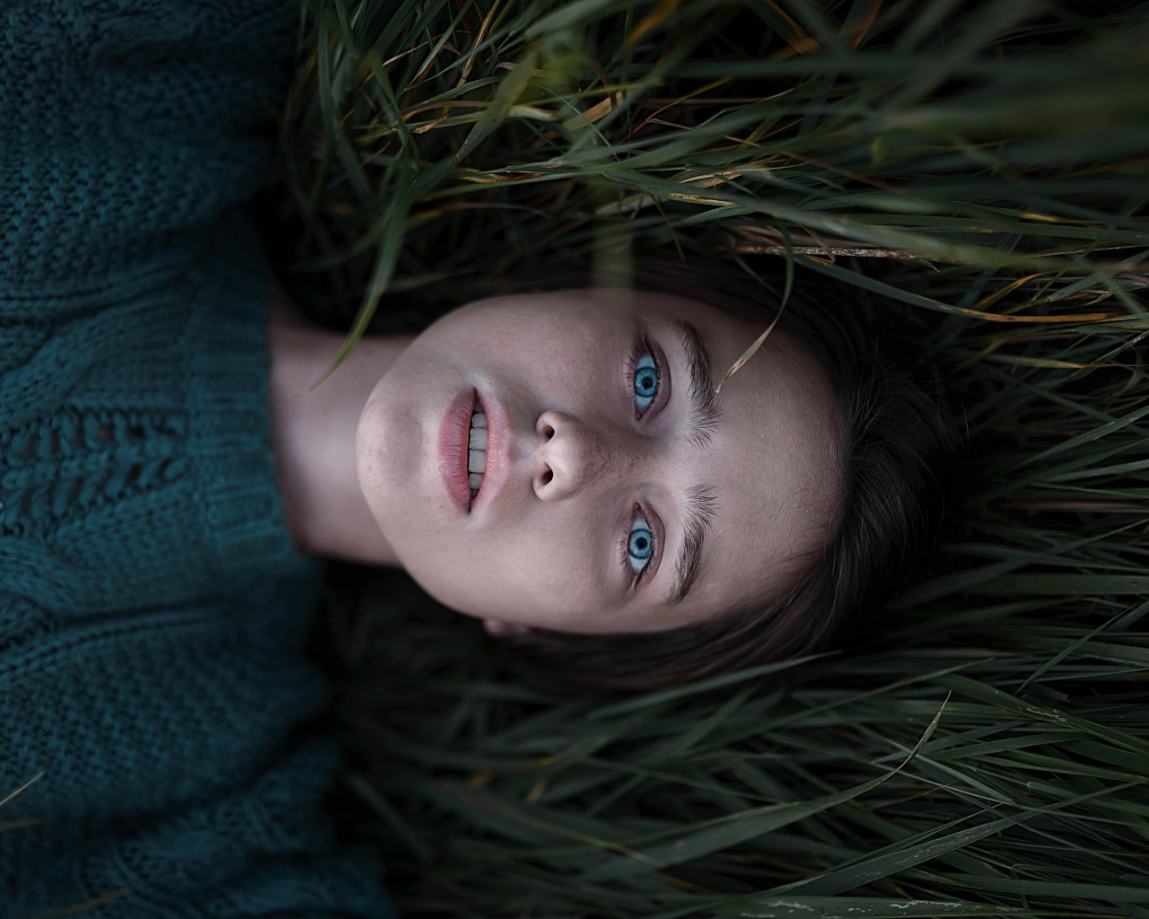 Голубоглазая девушка в свитере лежит на траве