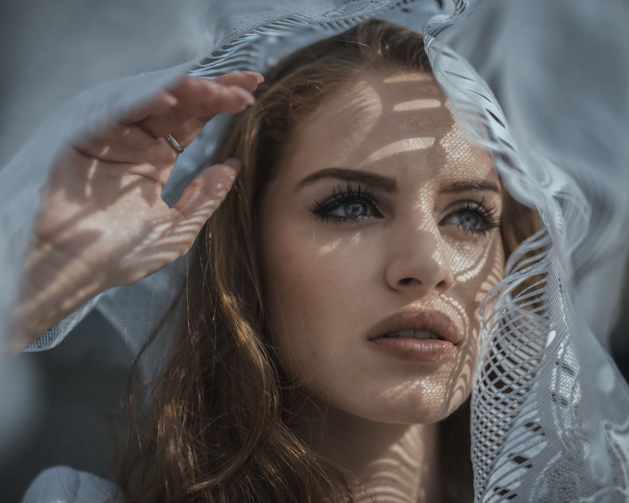 Голубоглазая девушка смотрит в окно с тюлью