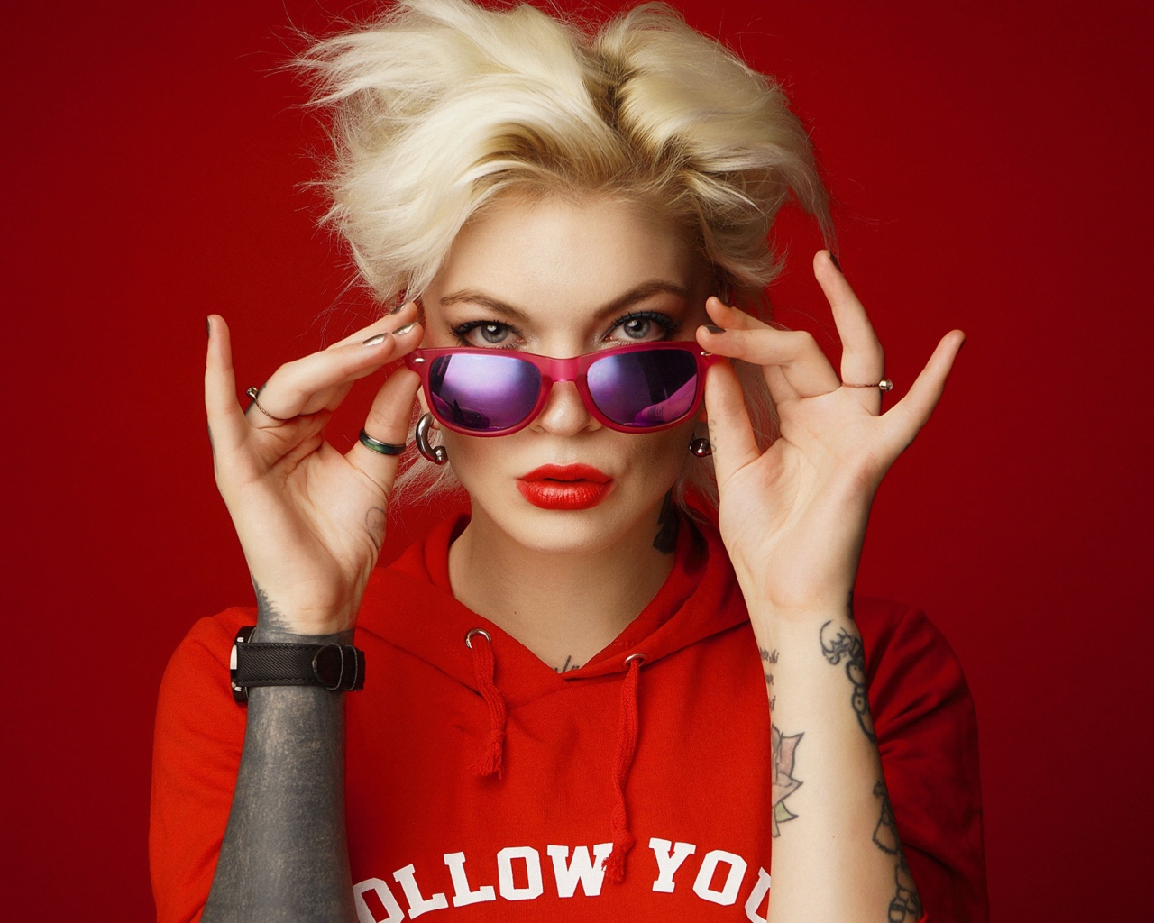Яркая блондинка с татуировками на руках на красном фоне