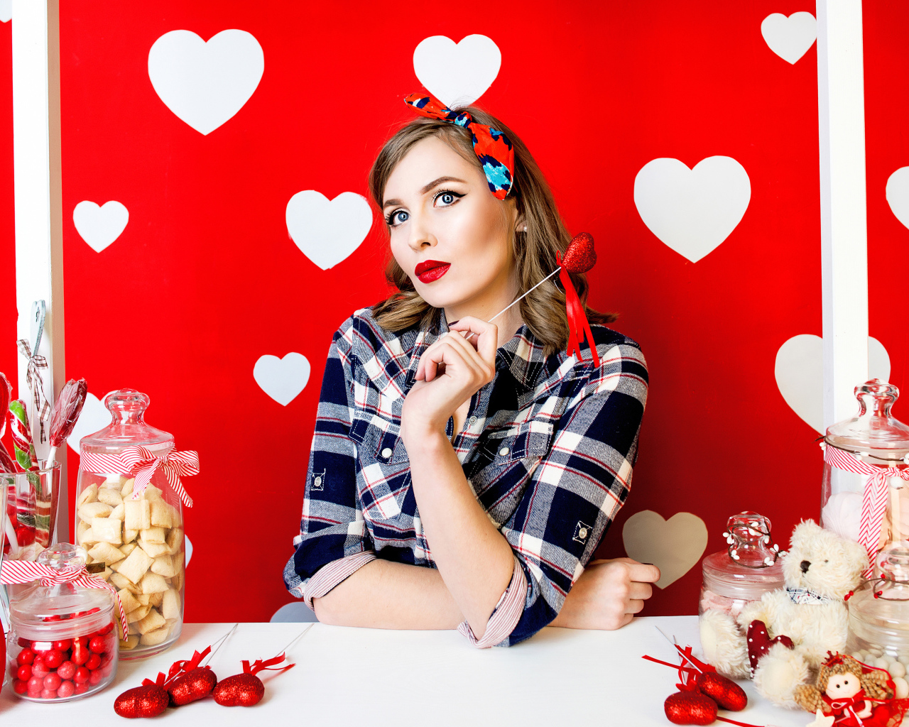 Яркая девушка за столом со сладостями на красном фоне с белыми сердечками 